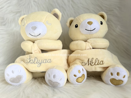 Deux oursons Jabar, l’un avec les yeux fermés et les pattes grises brodé avec un prénom au fil argenté et l’autre aux yeux ouverts, pattes dorées et brodé avec un prénom avec du fil doré